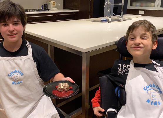 Two boys in aprons with one holding a piece of chocolate lava cake