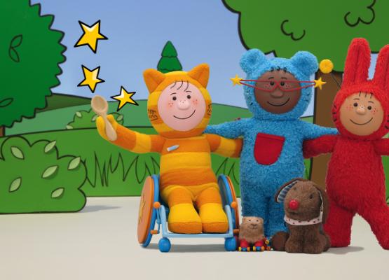 An orange cat in a wheelchair and a blue bear with big red glasses and a red rabbit with antennae are in a park