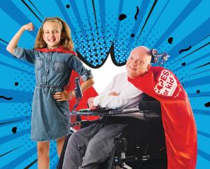 A child and an adult on wheelchair with red capes on