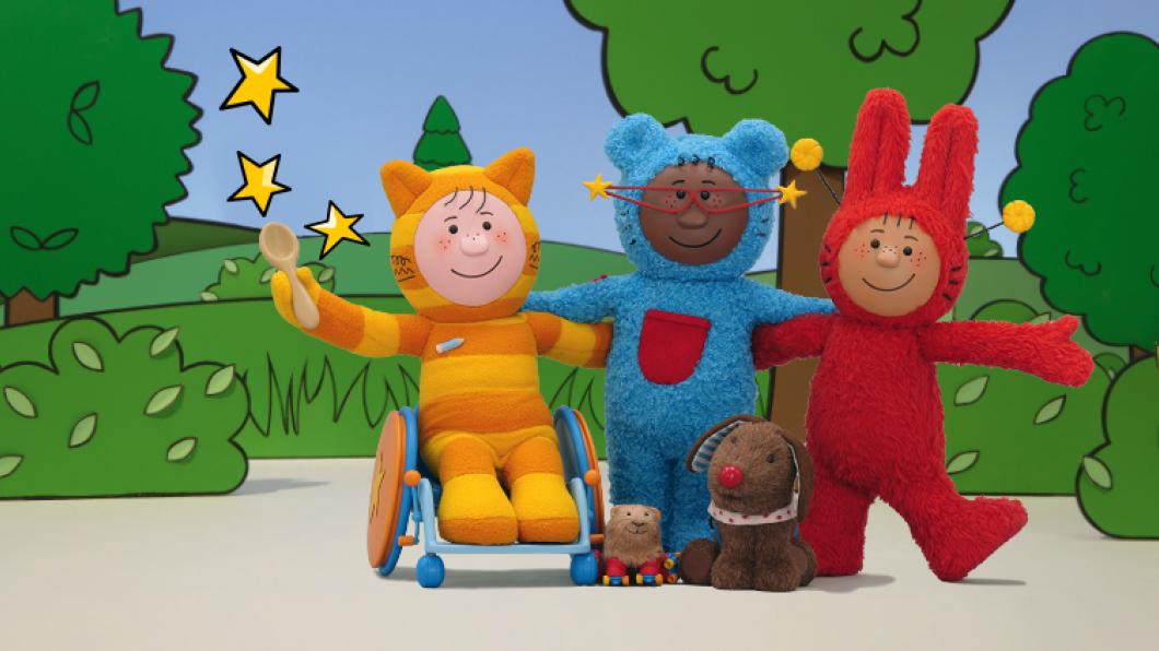 An orange cat in a wheelchair and a blue bear with big red glasses and a red rabbit with antennae are in a park