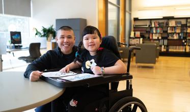 A child sitting on a wheelchair, accompany with an adult with smile