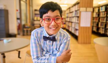 A child with big smile on face, wearing glasses with a library background