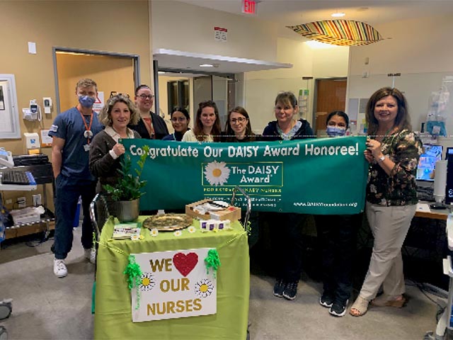 A group of nurses and hospital staffs holding a banner saying &quot;congratulate our Daisy Award honoree!