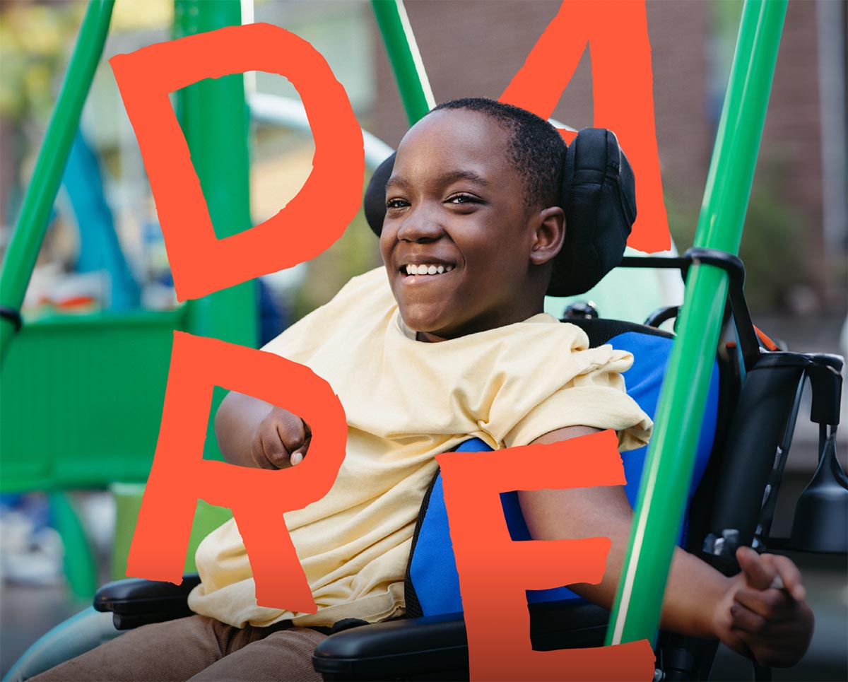 A children sitting on a wheelchair, with the word -DARE- around him