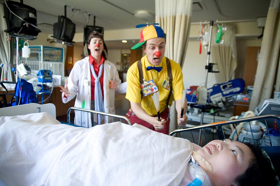Two clowns playing with a patient on the bed