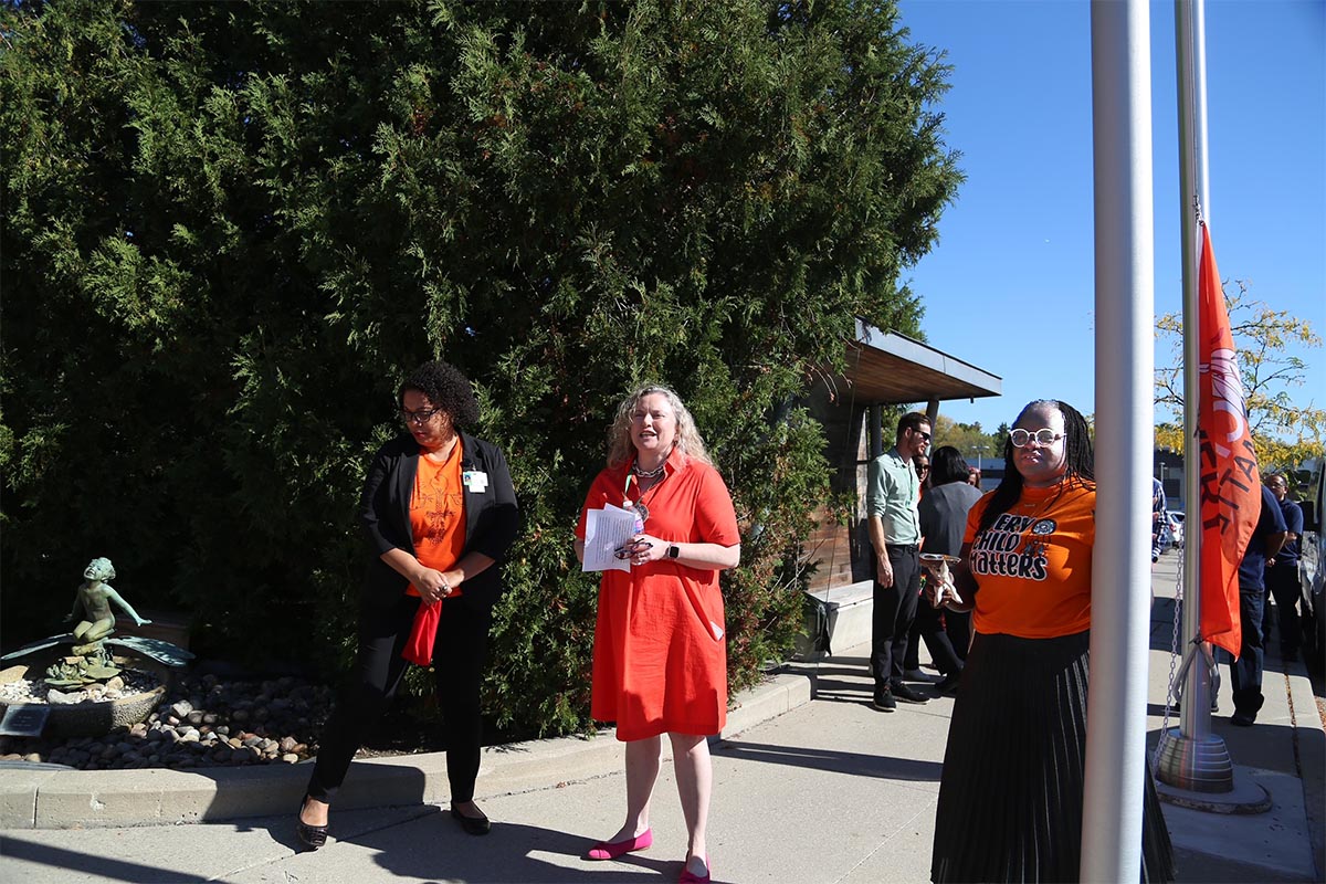 Three people dress in orange preparing for a flag raising ceremony