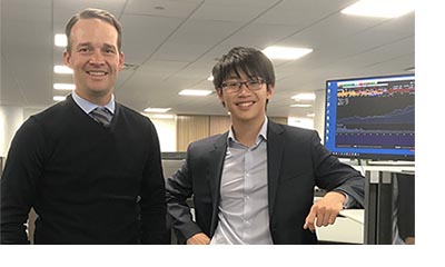 Two adults standing beside a computer