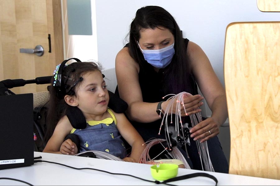 A woman holding some optical fiber wires and connecting to a brain scanning machine