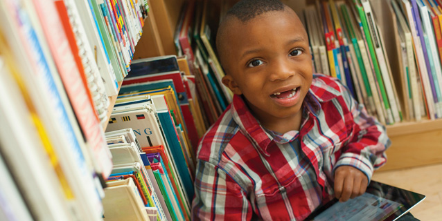 Little boy in library with computer tablet.