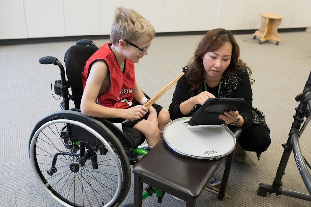woman helping boy in wheelchair to play drums