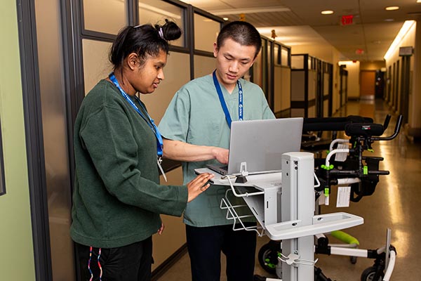 Two young workers with disabilities collaborate over a computer in a hallway.