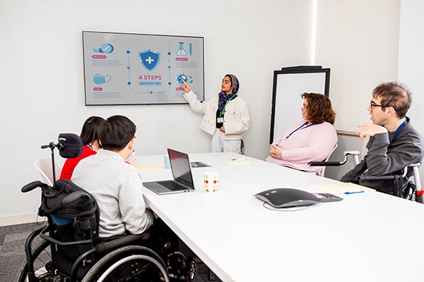 A young woman with a disability presents to a team of employees with diverse abilities