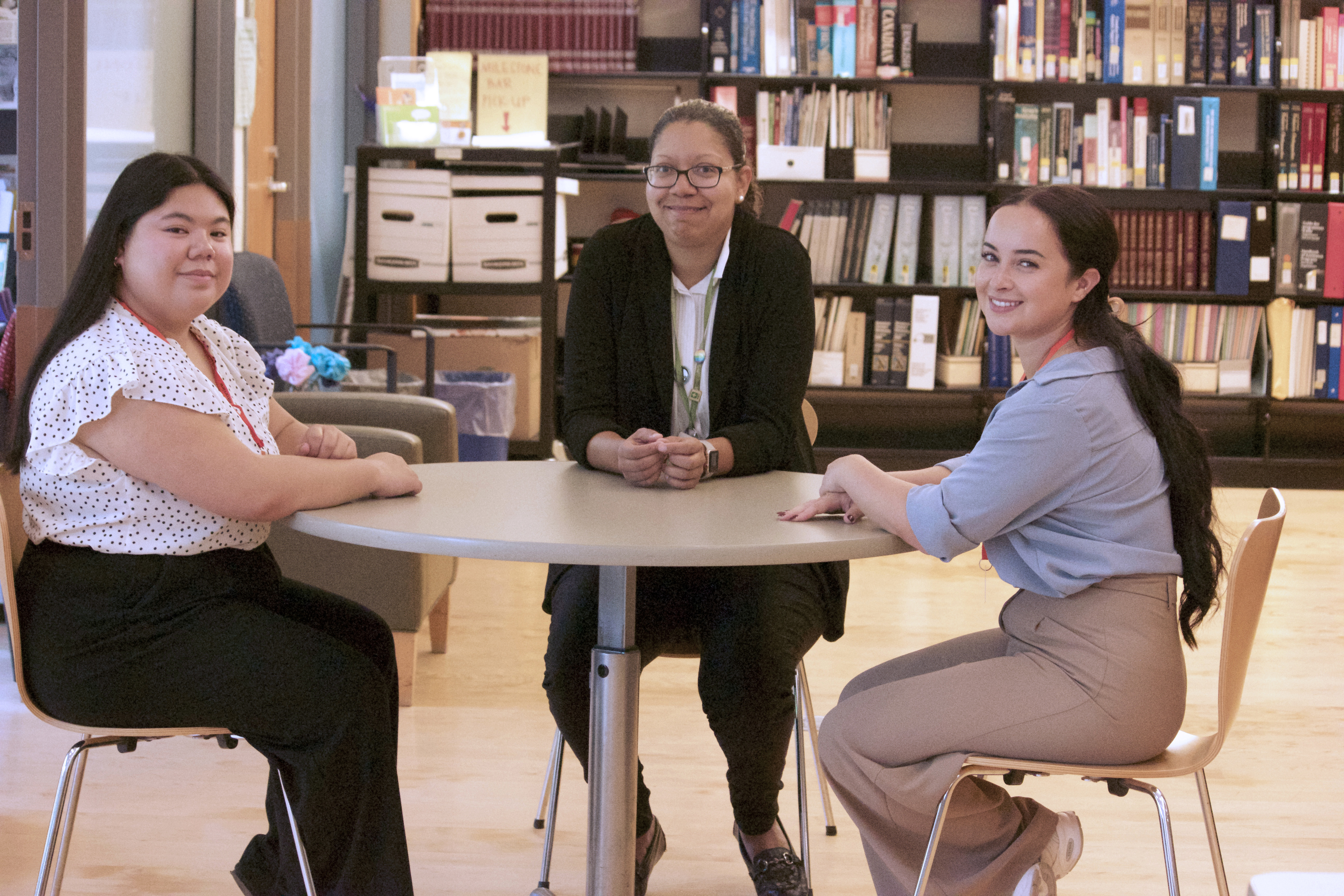 Three women sit around a table in the library