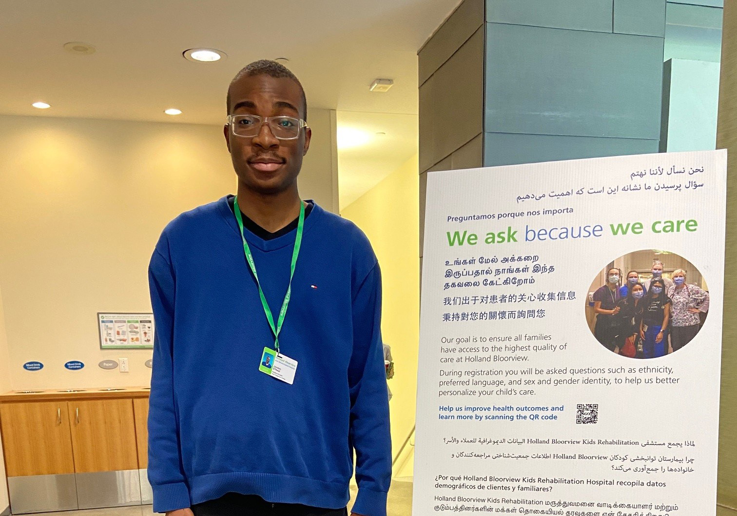 Jordan, standing beside an easel that reads: 'We ask because we care' in different languages