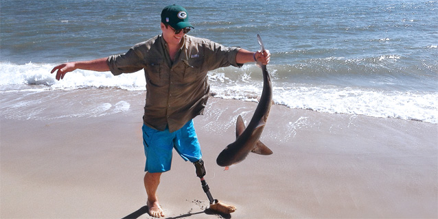 Man with prosthetic leg on the beach holding a fish.