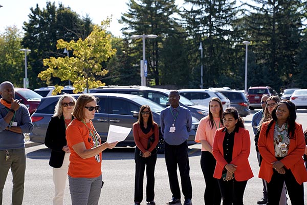 A group of people standing at a parking lot, in orange outfit