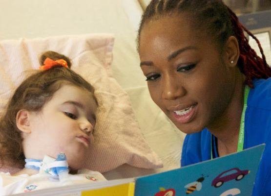 Nurse reads a book to young child with ventilator