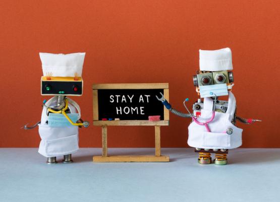 Two robots dressed as doctors with Stay at Home sign
