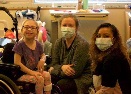 Girl in wheelchair with mother and nurse in masks smiling