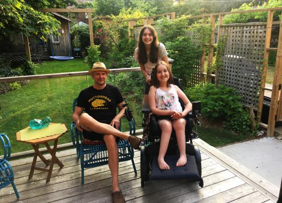 Father and two daughters, one in a wheelchair, on the back garden porch