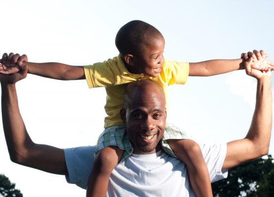 Dad holding young boy on shoulders with arms spread out