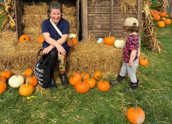 Woman on hay bail with flowers on prosthetic leg and small child nearby with pumpkins