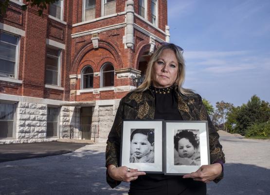 Blonde woman standing in front of institution holding photos of two young boys