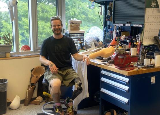 Man with beard and prosthetic leg sits on chair beside work table with tools