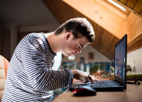 Young man bends over typing at computer