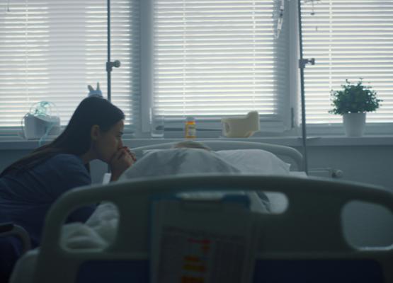 Mother with long black hair reaching over hospital bed to patient