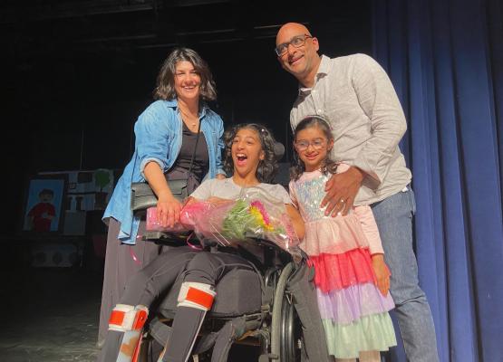 Teen in wheelchair holding flowers on stage surrounded by her family