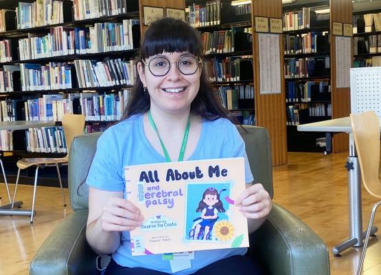 Woman with long dark hair in blue t shirt holds children's book and smiles