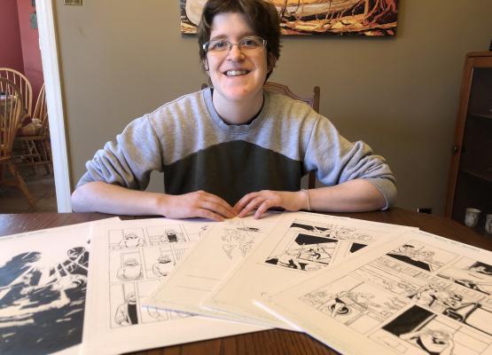 Woman sits at table where a series of comics panels are displayed