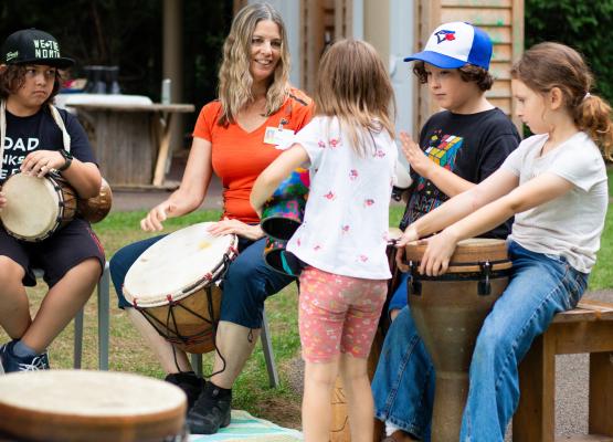 Woman with long hair plays drum in the middle of a drum circle with children