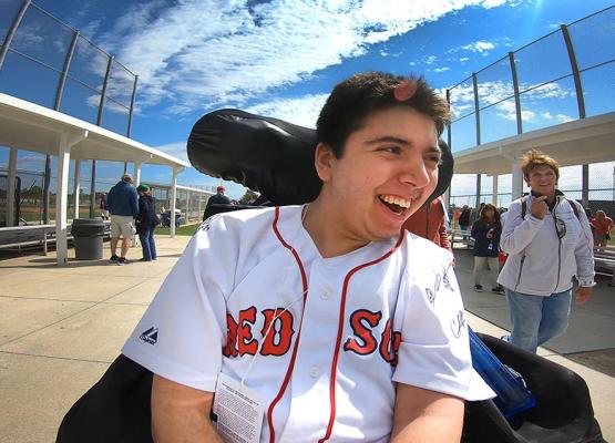 Young man with dark hair in Red Sox shirt smiles in wheelchair