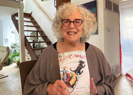 Woman with wavy white hair holds children's book