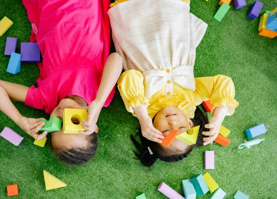 Two young children lie on the floor and play with blocks