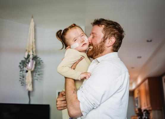Man with beard hugs small girl with pony tails and nasal prongs