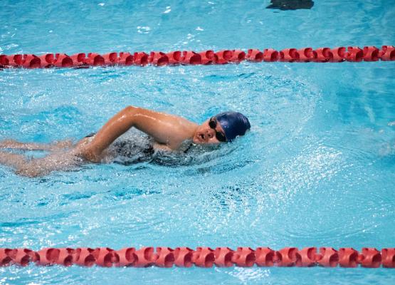 Woman in blue cap and black goggles swims the front crawl in a pool lane with red dividers