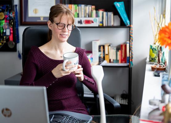 Woman with glasses and burgundy sweater holds mug in office