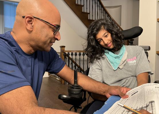 Bald man with glasses goes through a homework sheet with teen with dark hair in wheelchair