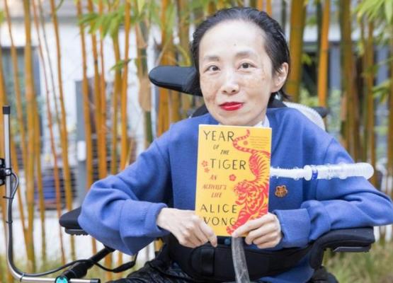 Woman in royal blue holding book called Year of the Tiger sits in wheelchair