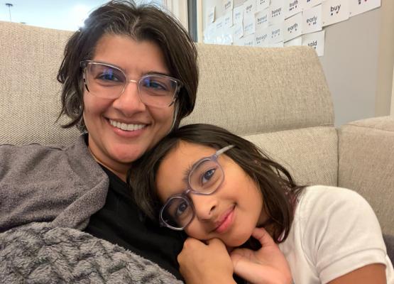 Woman with dark hair and glasses snuggles with girl with dark hair and glasses