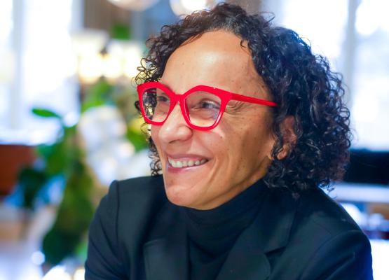 Woman with black curly hair and red glasses smiles to the side