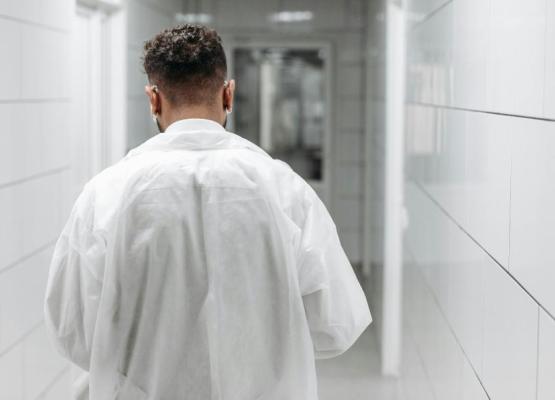 Man in white doctor's coat walks down hospital hall