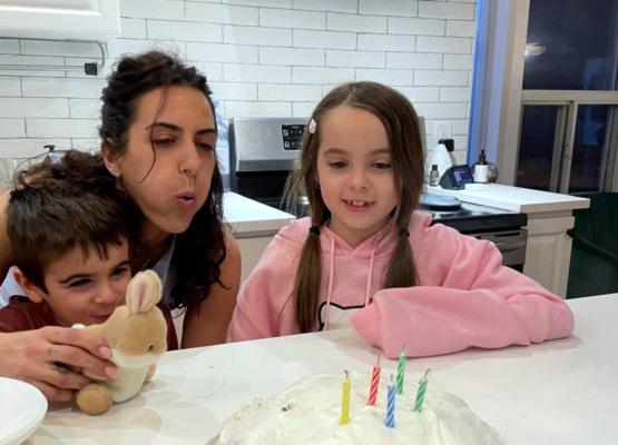 Woman inbetween a girl and boy blowing out candles on a cake