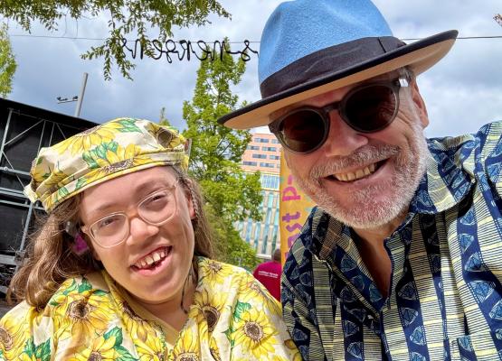 Girl with yellow sunflower hat and shirt smiles with man with blue brimmed hat and sun glasses