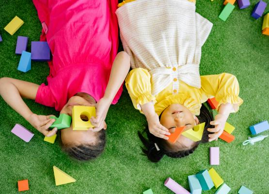 Young girls lie on floor playing with blocks
