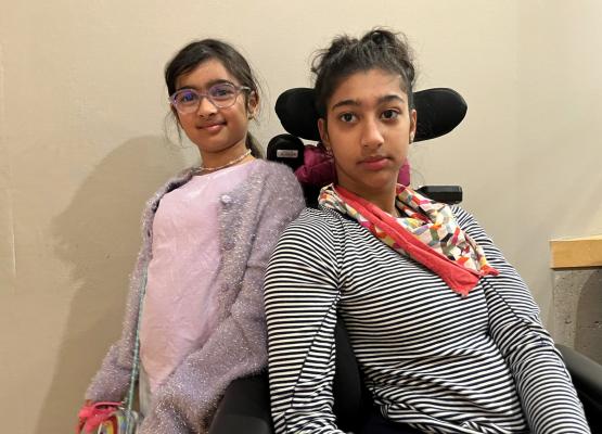 Teen with dark hair and red scarf in wheelchair beside girl with dark hair and pink shirt