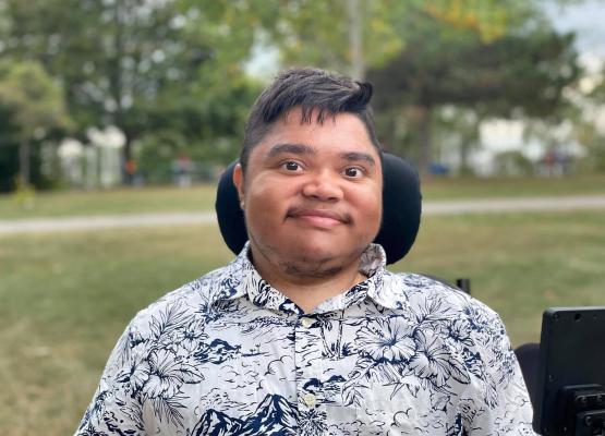 Man with dark hair in wheelchair smiles in park